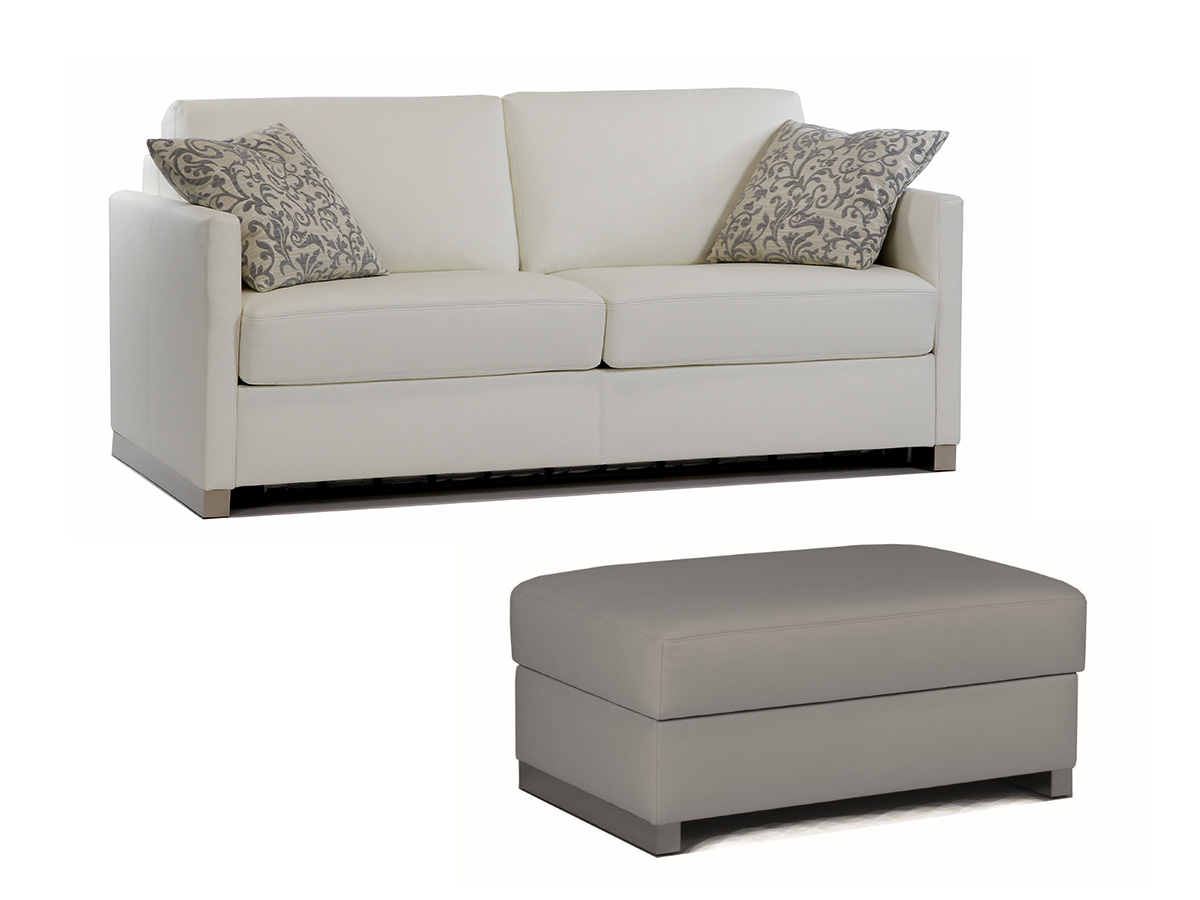 Schlafsofa Cube in cremefarbenem Bezug mit zwei Zierkissen und passendem Hocker vor weißem Hintergrund